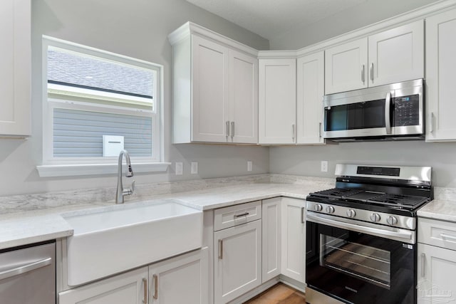 kitchen featuring a sink, stainless steel appliances, light stone counters, and white cabinets