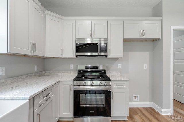 kitchen featuring light stone counters, baseboards, light wood-style flooring, appliances with stainless steel finishes, and white cabinetry