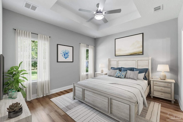 bedroom with a tray ceiling, baseboards, visible vents, and wood finished floors