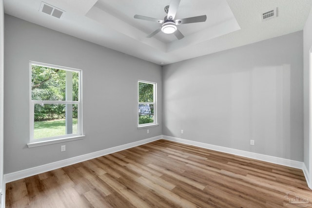 empty room featuring a tray ceiling, wood finished floors, baseboards, and visible vents