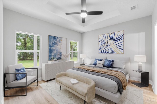 bedroom with visible vents, baseboards, light wood finished floors, a raised ceiling, and ceiling fan