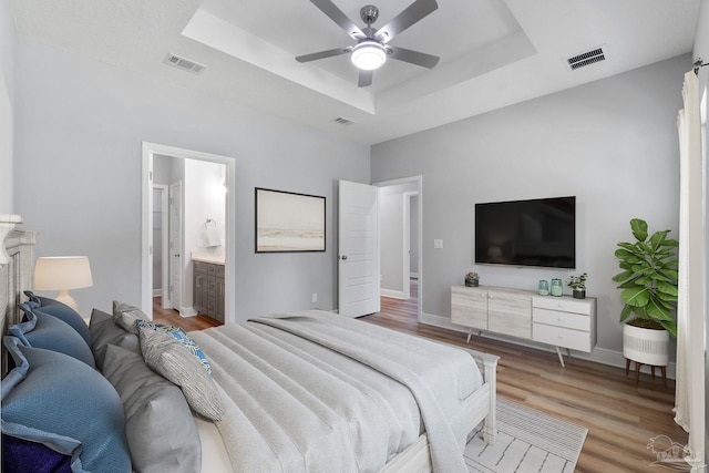 bedroom featuring a tray ceiling, visible vents, and light wood finished floors