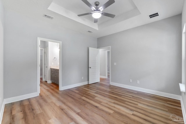 unfurnished bedroom with a raised ceiling, light wood-style floors, visible vents, and baseboards