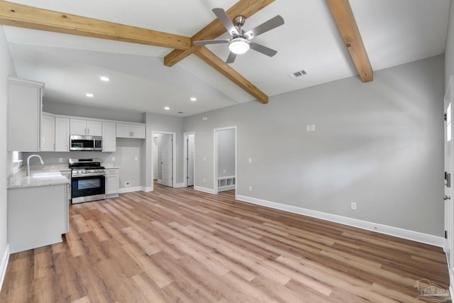 kitchen with light wood finished floors, baseboards, appliances with stainless steel finishes, white cabinets, and a sink