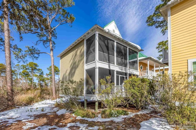 snow covered back of property with a sunroom