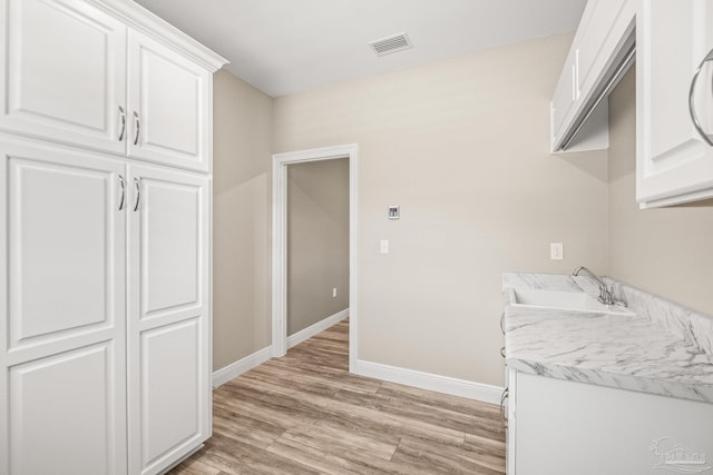 kitchen with baseboards, visible vents, a sink, white cabinetry, and light wood-style floors