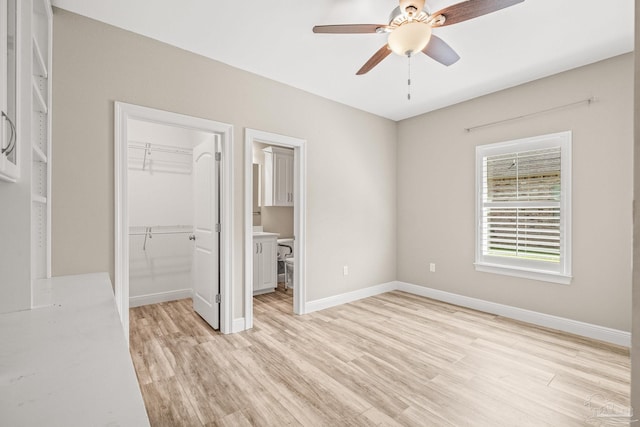 unfurnished bedroom with baseboards, a walk in closet, a closet, and light wood-type flooring