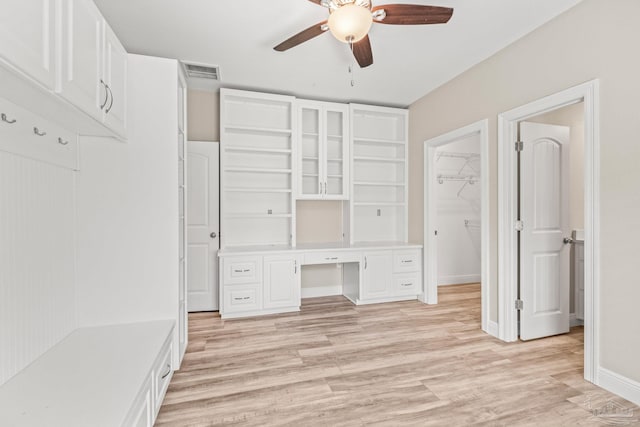 interior space featuring light wood-style flooring, baseboards, ceiling fan, visible vents, and built in desk