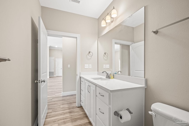 half bathroom featuring baseboards, visible vents, toilet, vanity, and wood finished floors