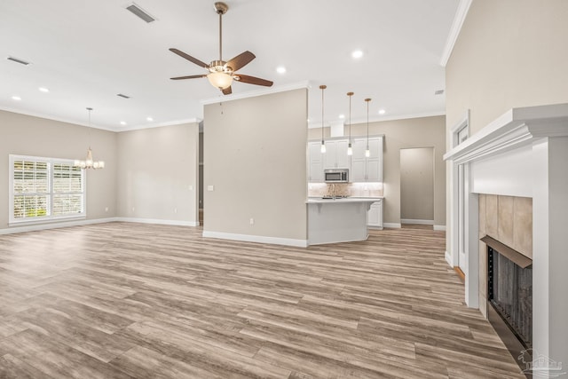 unfurnished living room with light wood-style flooring, baseboards, visible vents, ceiling fan with notable chandelier, and a tiled fireplace