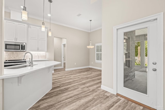 kitchen featuring light countertops, stainless steel microwave, a sink, decorative light fixtures, and white cabinetry