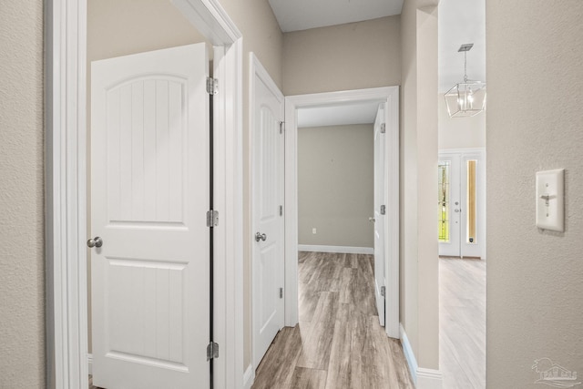 corridor with light hardwood / wood-style flooring and a notable chandelier