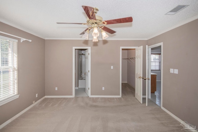 unfurnished bedroom with a textured ceiling, light carpet, a walk in closet, and ceiling fan