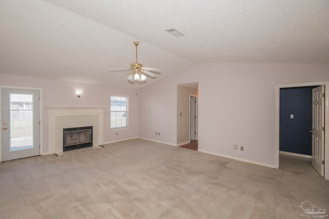 unfurnished living room featuring lofted ceiling, a tile fireplace, light colored carpet, a textured ceiling, and ceiling fan