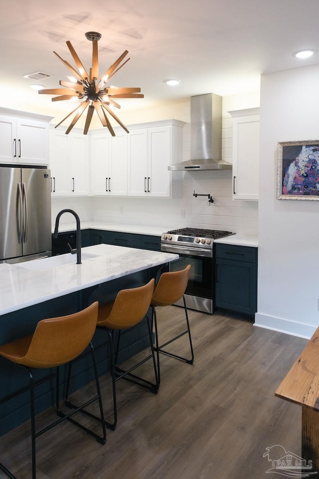 kitchen with wall chimney range hood, a breakfast bar area, appliances with stainless steel finishes, white cabinets, and dark wood-style flooring