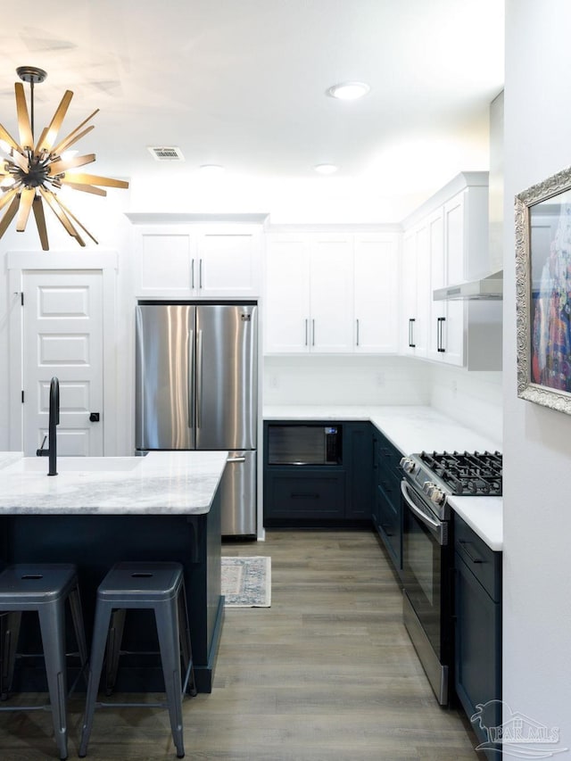 kitchen featuring a kitchen bar, light wood-style flooring, white cabinets, stainless steel appliances, and wall chimney exhaust hood