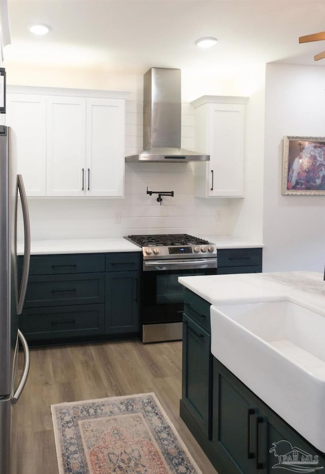 kitchen featuring white cabinets, appliances with stainless steel finishes, wall chimney exhaust hood, and wood finished floors