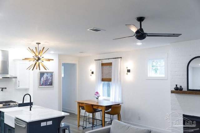 kitchen featuring stainless steel gas range oven, visible vents, ceiling fan with notable chandelier, white cabinetry, and wall chimney exhaust hood