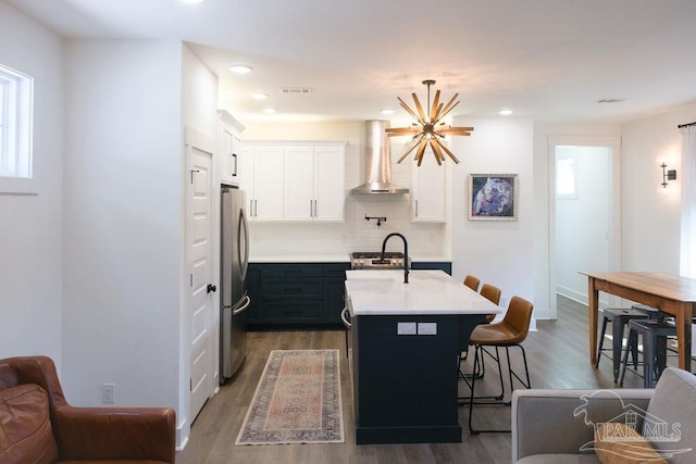 kitchen featuring visible vents, a breakfast bar area, light countertops, freestanding refrigerator, and wall chimney exhaust hood