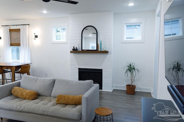 living area featuring a brick fireplace, dark wood-type flooring, baseboards, ceiling fan, and recessed lighting