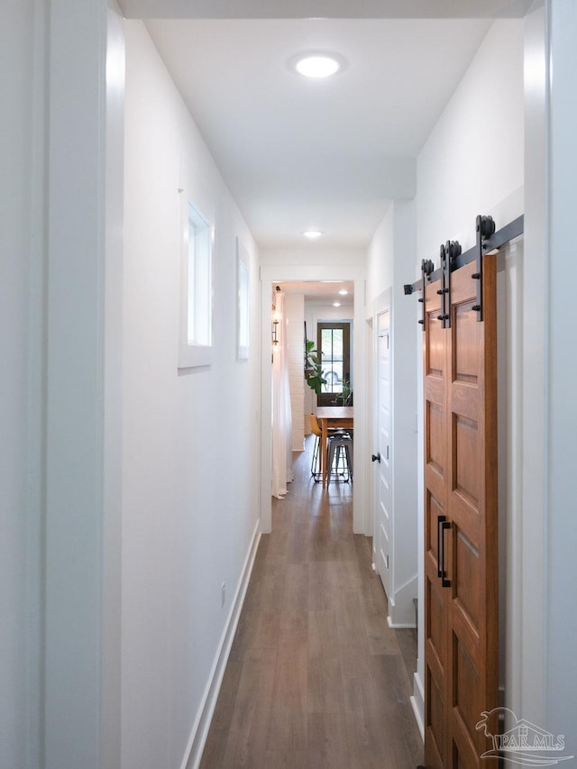 hall with dark wood-style floors, a barn door, and baseboards