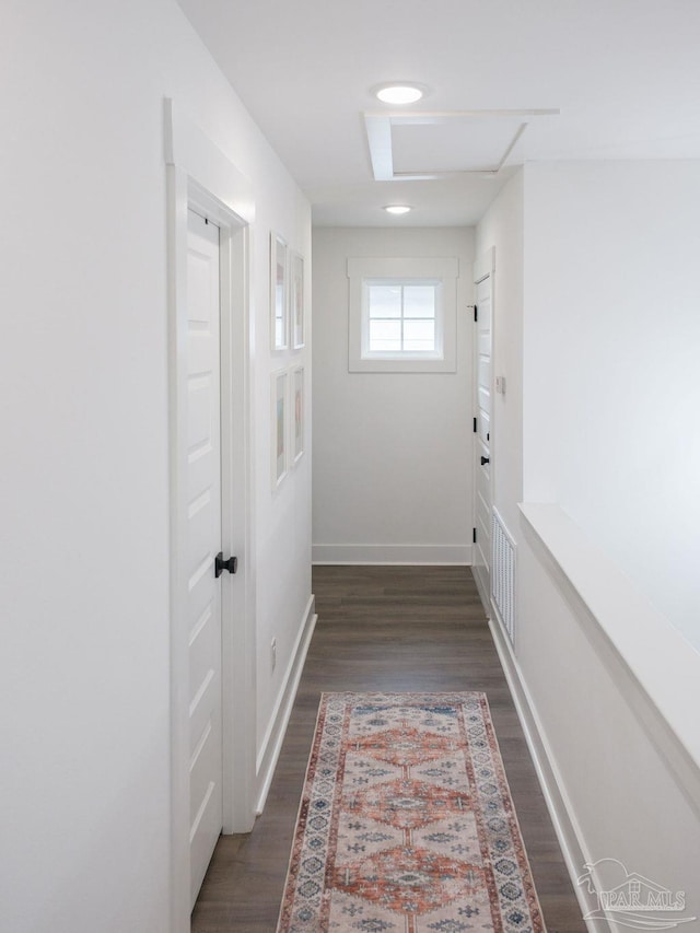 hall with visible vents, baseboards, and dark wood-style flooring