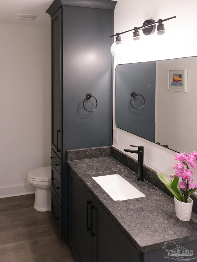 bathroom featuring visible vents, baseboards, toilet, wood finished floors, and vanity