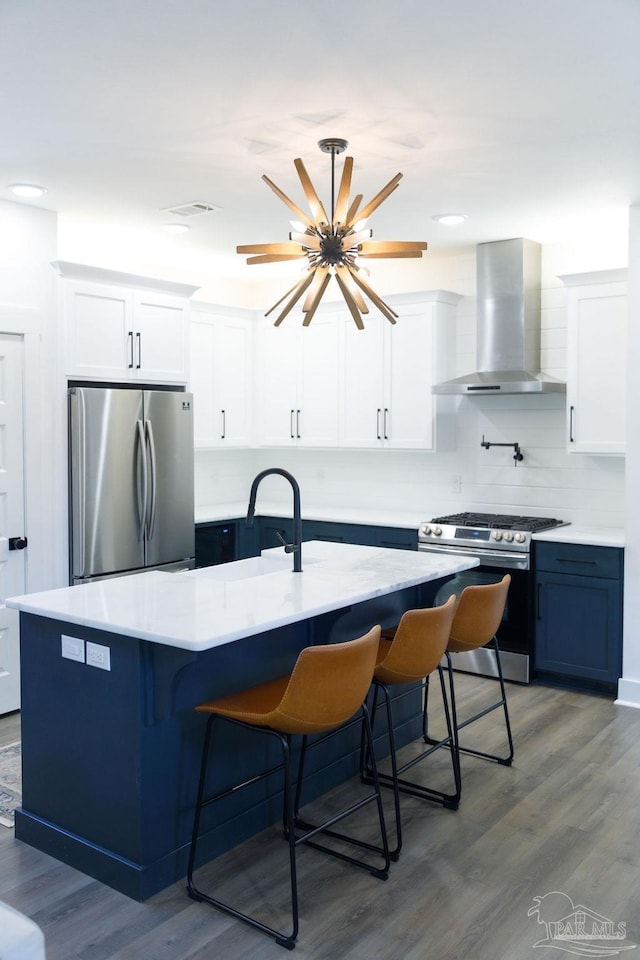 kitchen with stainless steel appliances, wall chimney exhaust hood, light countertops, and wood finished floors