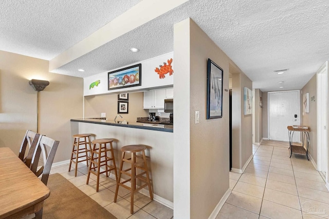 interior space with a textured ceiling, kitchen peninsula, white cabinets, and light tile patterned flooring