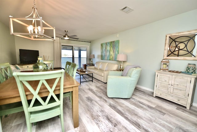 living room featuring ceiling fan with notable chandelier and light wood-type flooring