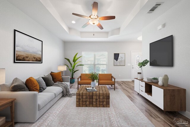 living room with ceiling fan, a raised ceiling, and light hardwood / wood-style flooring