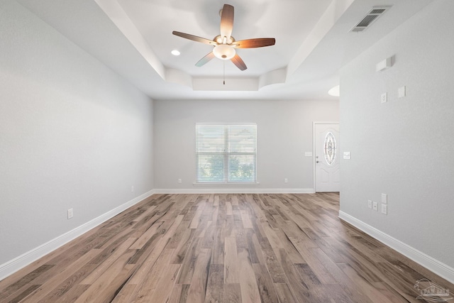 empty room with ceiling fan, wood-type flooring, and a tray ceiling