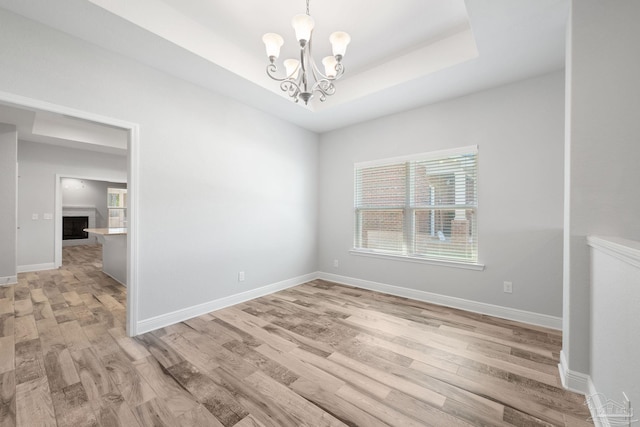 unfurnished room featuring a tray ceiling, light hardwood / wood-style flooring, and an inviting chandelier