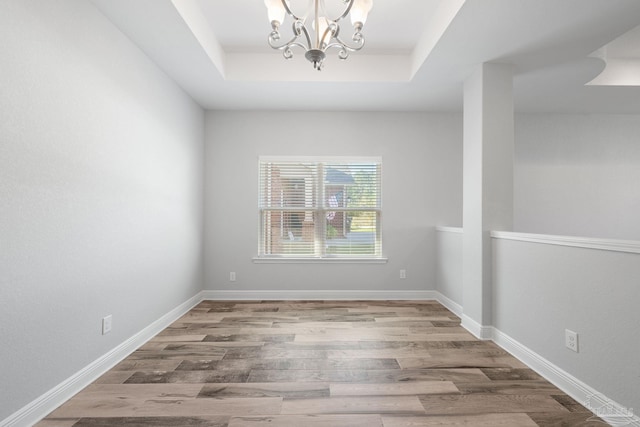 empty room with a chandelier, hardwood / wood-style flooring, and a tray ceiling