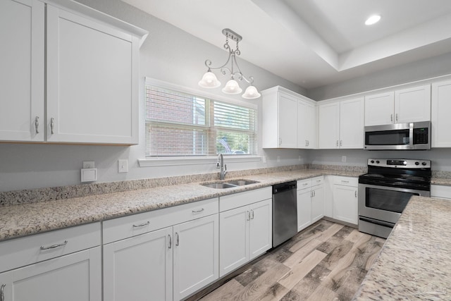 kitchen with appliances with stainless steel finishes, sink, white cabinetry, pendant lighting, and light hardwood / wood-style flooring