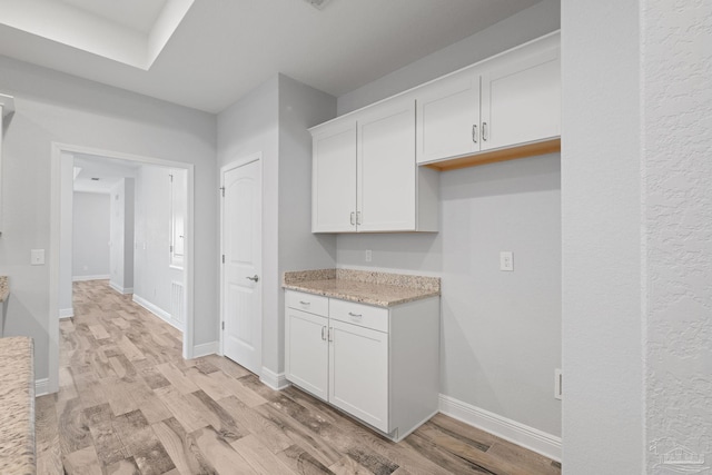 kitchen featuring white cabinetry, light stone countertops, and light wood-type flooring