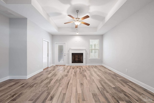 unfurnished living room with ceiling fan, light wood-type flooring, and a raised ceiling