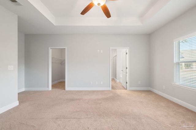 unfurnished bedroom with a spacious closet, light colored carpet, a tray ceiling, and ceiling fan