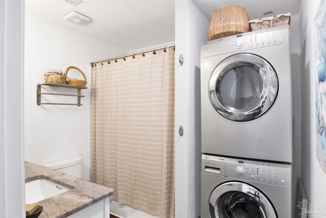 clothes washing area with a textured ceiling and stacked washer and dryer