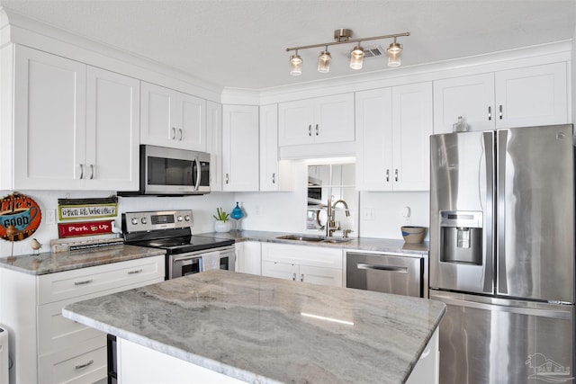 kitchen with light stone countertops, appliances with stainless steel finishes, a kitchen island, sink, and white cabinetry