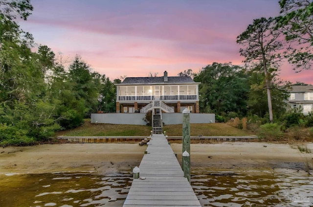 back of property at dusk with a chimney, a sunroom, a water view, and stairway