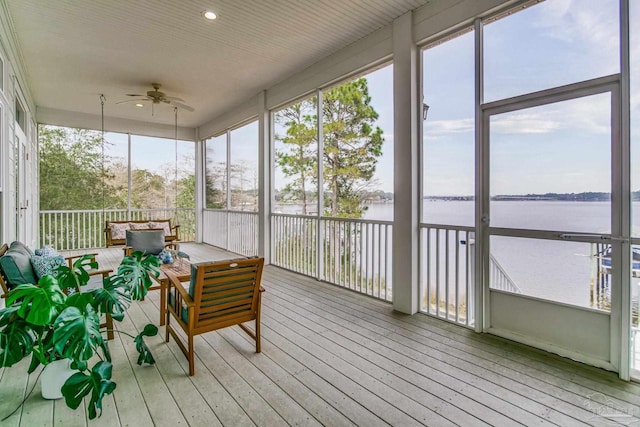 sunroom with plenty of natural light, a water view, and a ceiling fan