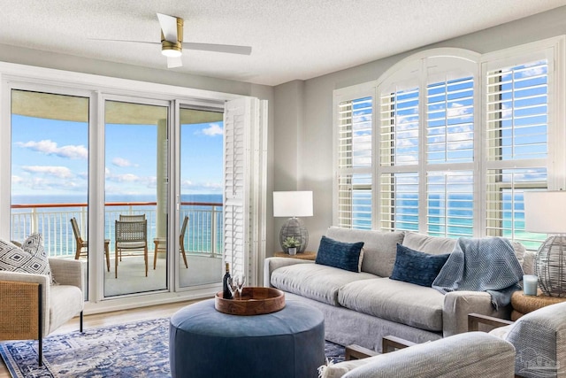 living room featuring a textured ceiling, a water view, wood-type flooring, and ceiling fan