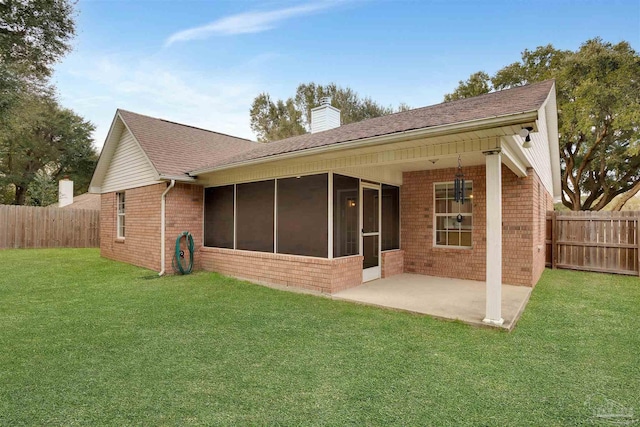 back of house featuring brick siding, a sunroom, a lawn, a chimney, and a patio area