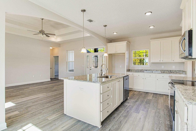 kitchen featuring light stone counters, light wood finished floors, a sink, appliances with stainless steel finishes, and white cabinetry