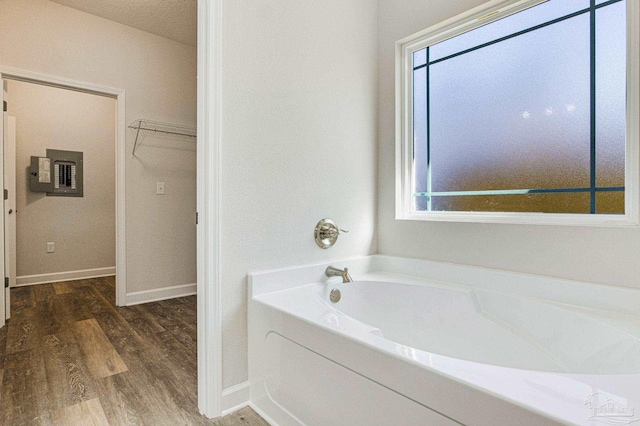 full bathroom featuring electric panel, plenty of natural light, a garden tub, and wood finished floors