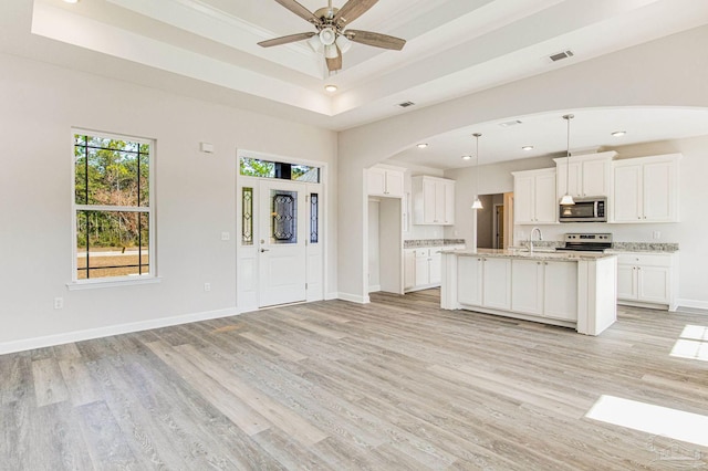 kitchen featuring baseboards, light wood finished floors, a sink, stainless steel appliances, and white cabinets