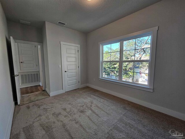 unfurnished bedroom featuring carpet, a textured ceiling, visible vents, and baseboards