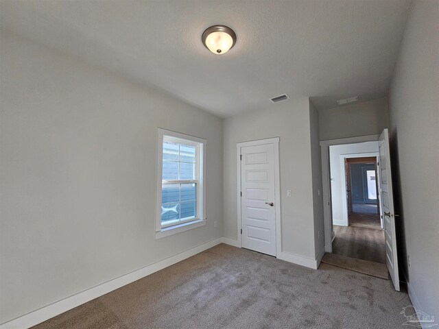 unfurnished bedroom with baseboards, a textured ceiling, visible vents, and light colored carpet