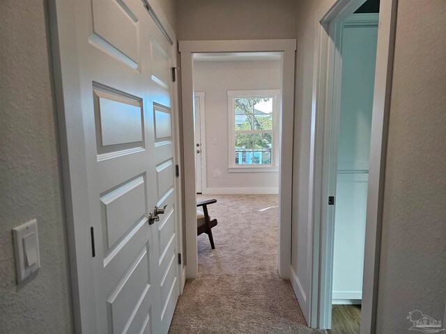 hallway featuring light colored carpet and baseboards